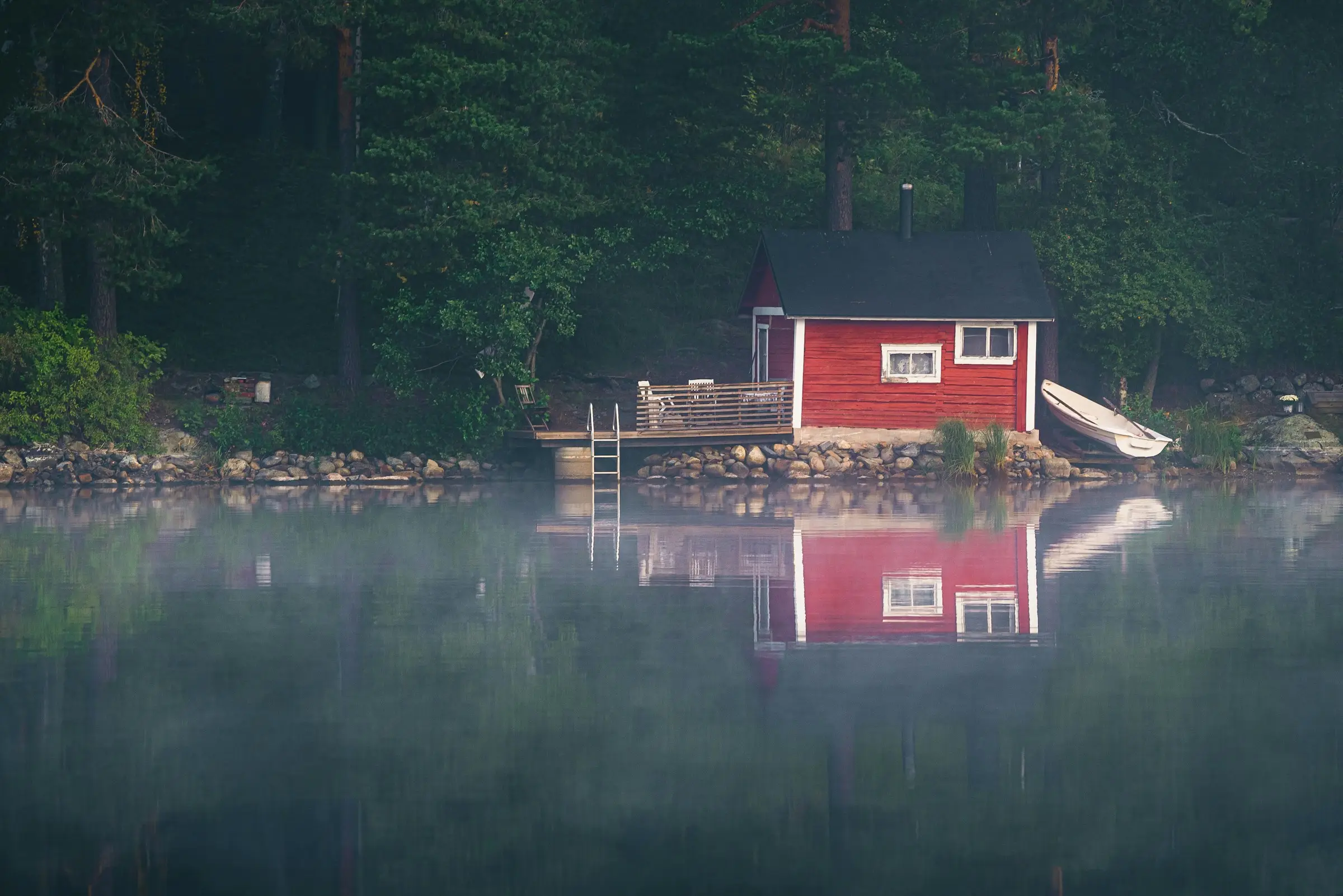 En röd bastu vid en stilla, dimmig sjö som speglar sig i vattnet